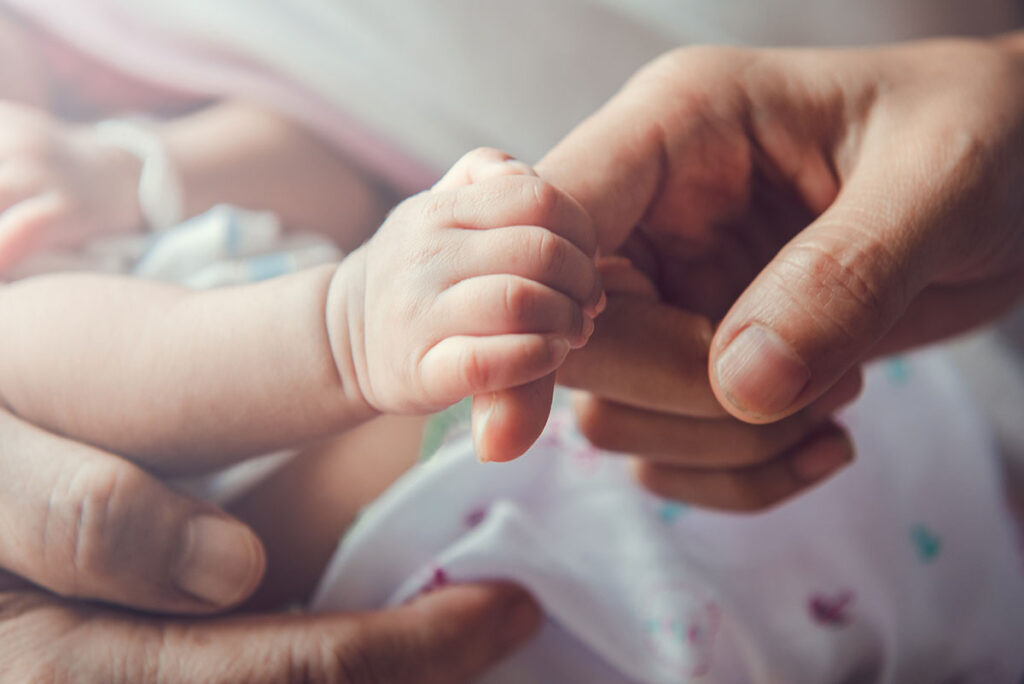 A baby's hand is holding a finger of the adult